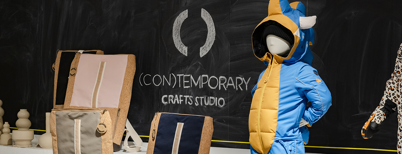 Keramikvasen, Rucksäcke und ein blau-gelber Schneeanzug mit Drachenkapuze vor einer großen Tafelwand mit der Aufschrift "(Con)Temporary Crafts Studio". - Quelle: WFB/Jan Rathke