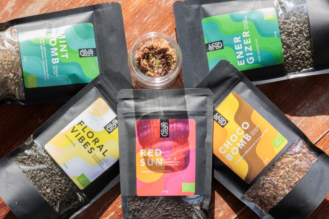Verschiedene Teesorten in schwarzen Verpackungen mit bunten Etiketten. Darauf steht Mint Bomb, Floral Vibes, Red Sun, Choco Bomb und Energizer.