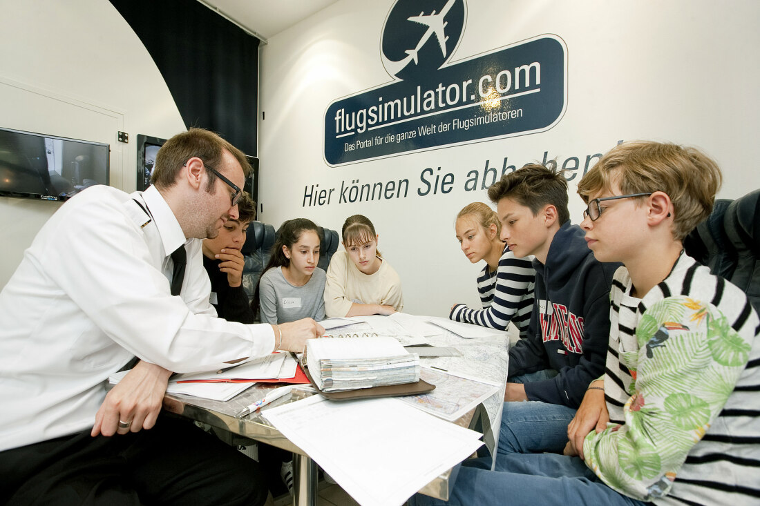 Ein Pilot sitzt an einem Tisch mit Kindern und erklärt ihnen etwas